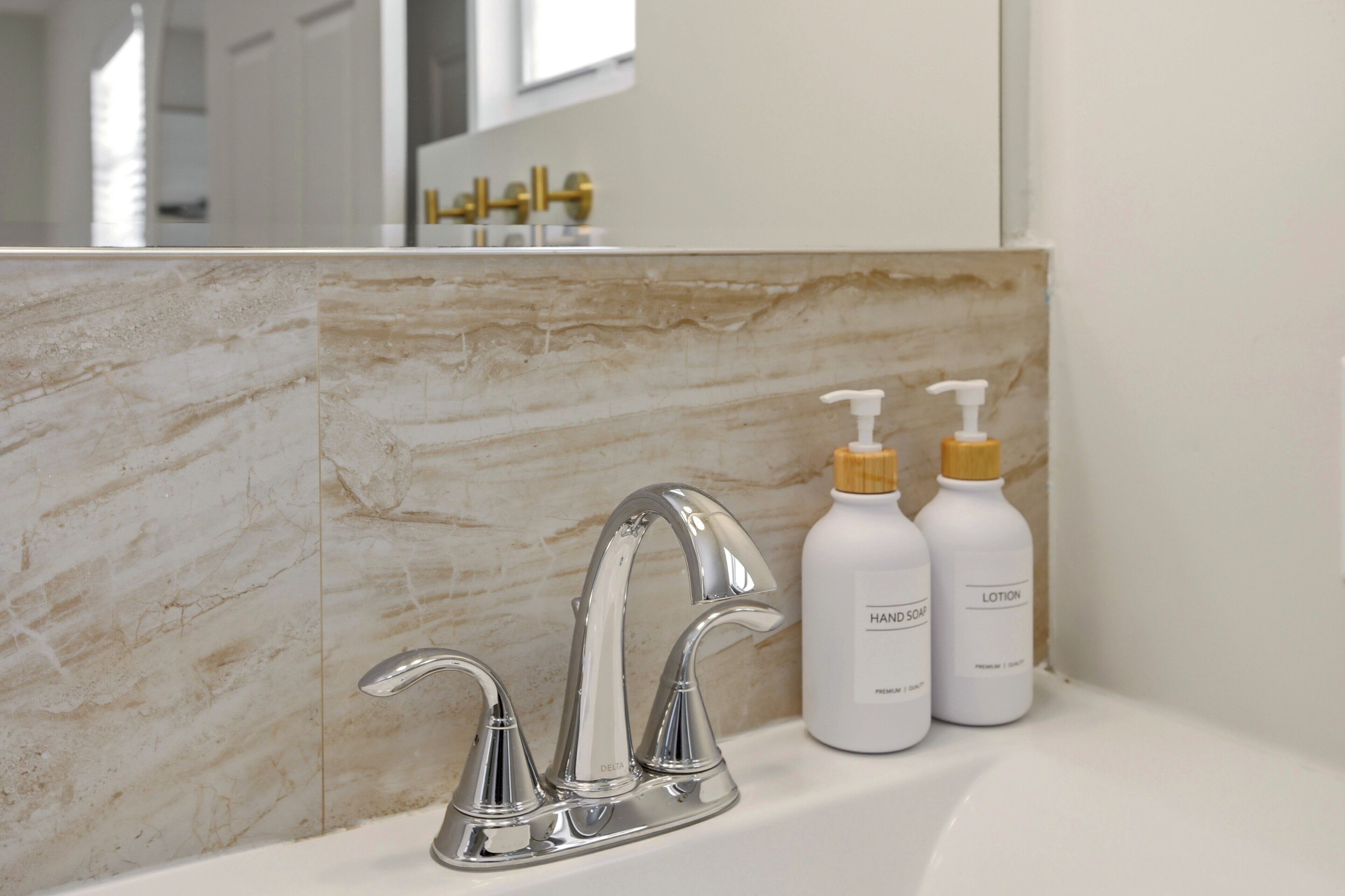 Une salle de bain avec un mur en marbre, un robinet moderne et deux flacons de savon liquide et de lotion pour les mains.