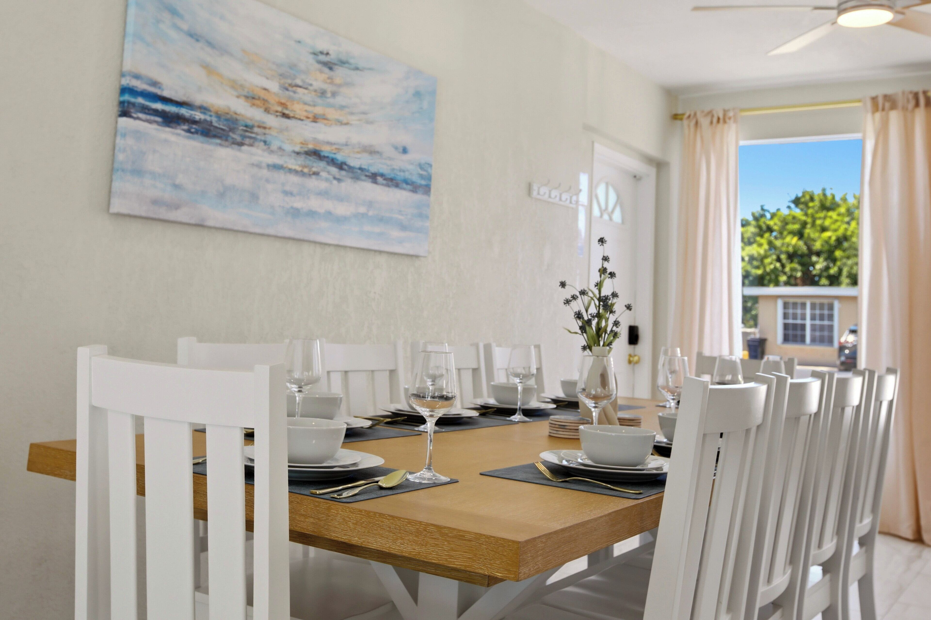 A dining area with a wooden table, white chairs, and a painting on the wall.