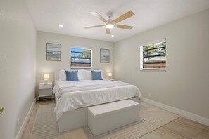 Ein Schlafzimmer mit Bett, einer Bank, einem Deckenventilator und zwei Fenstern mit Jalousien.