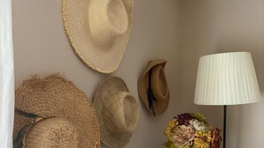 A wall with several straw hats and a lamp with a floral arrangement on a dresser.