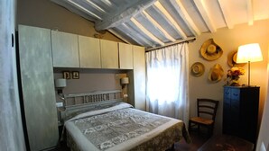 A bedroom with a bed, a desk, a chair, a lamp, and a wall with hats.