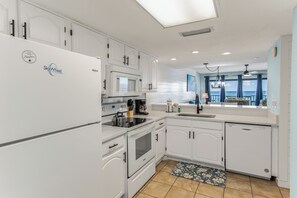 A modern kitchen with white cabinetry, a built-in microwave, and a dishwasher. - Wrap around Views! Newly Remodeled 9th Floor 3BR 3BA Commodore *BEACH CHAIRS! (Panama City Beach)