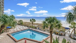 Ein Poolbereich mit Blick auf Strand und Meer, umgeben von Palmen und Liegestühlen.