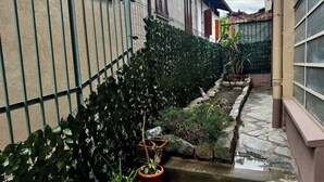 Un callejón estrecho con cerca metálica, una fuente pequeña y plantas en macetas.