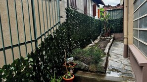 A narrow alley with a metal fence, a small water feature, and potted plants. - Charming Apartment with Wood Fireplace, Garden & Mountain View near Oropa (Biella)