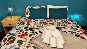 Una cama con una colcha estampada, dos almohadas, una lámpara de noche y una toalla doblada.