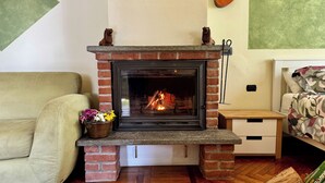 Una chimenea con revestimiento de ladrillo, un florero sobre la repisa, una mesita de noche de madera, una cama con ropa de cama floral y un sofá.