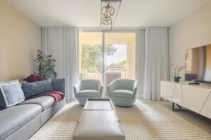 Ein modernes Wohnzimmer mit einer Couch, zwei Sesseln, einem Couchtisch, einem Fernseher und Blick auf einen Balkon.