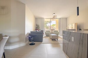 Ein modernes Wohnzimmer mit einer Couch, Sesseln, einem kleinen Tisch und einer Küchenzeile mit Marmorarbeitsplatte.