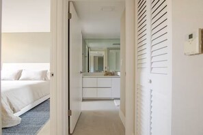 Ein Hotelzimmer mit Bett, einem Badezimmer inklusive Spiegel und einem Flur, der zu einem weiteren Zimmer führt.