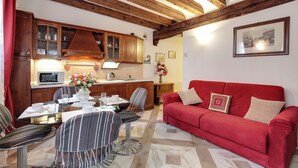 A cozy living room with a red sofa and striped chairs, a wooden ceiling, and a kitchen area with wooden cabinets and a microwave. - ANGELS' HOUSE (Venezia)