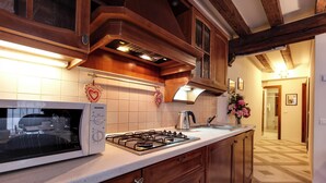 A kitchen with wooden cabinets, a white microwave, and a gas stove. - ANGELS' HOUSE (Venezia)