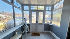 A sunroom with large windows, a bench, a door with a doormat, and a decorative vase. - Birmingham Contractor Stay, 5 Bed, Private Parking, Near M6, Groups (Birmingham)