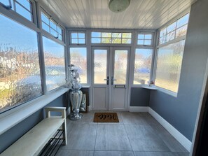 A sunroom with large windows, a bench, a door with a doormat, and a decorative vase. - Birmingham Contractor Stay, 5 Bed, Private Parking, Near M6, Groups (Birmingham)