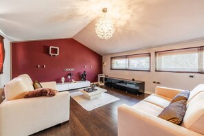 Ein modernes Wohnzimmer mit roter Akzentwand, einem weißen Sofa, einem beigen Sofa und einem großen Fernseher.