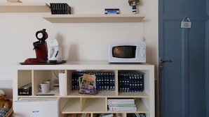 A room with a white microwave, a red coffee maker, and a bookshelf with books and magazines. - Bed and Breakfast 'Chambre Bleue' with Private Garden, Wi-Fi and Air Conditioning (Saint Aulaye-Puymangou)
