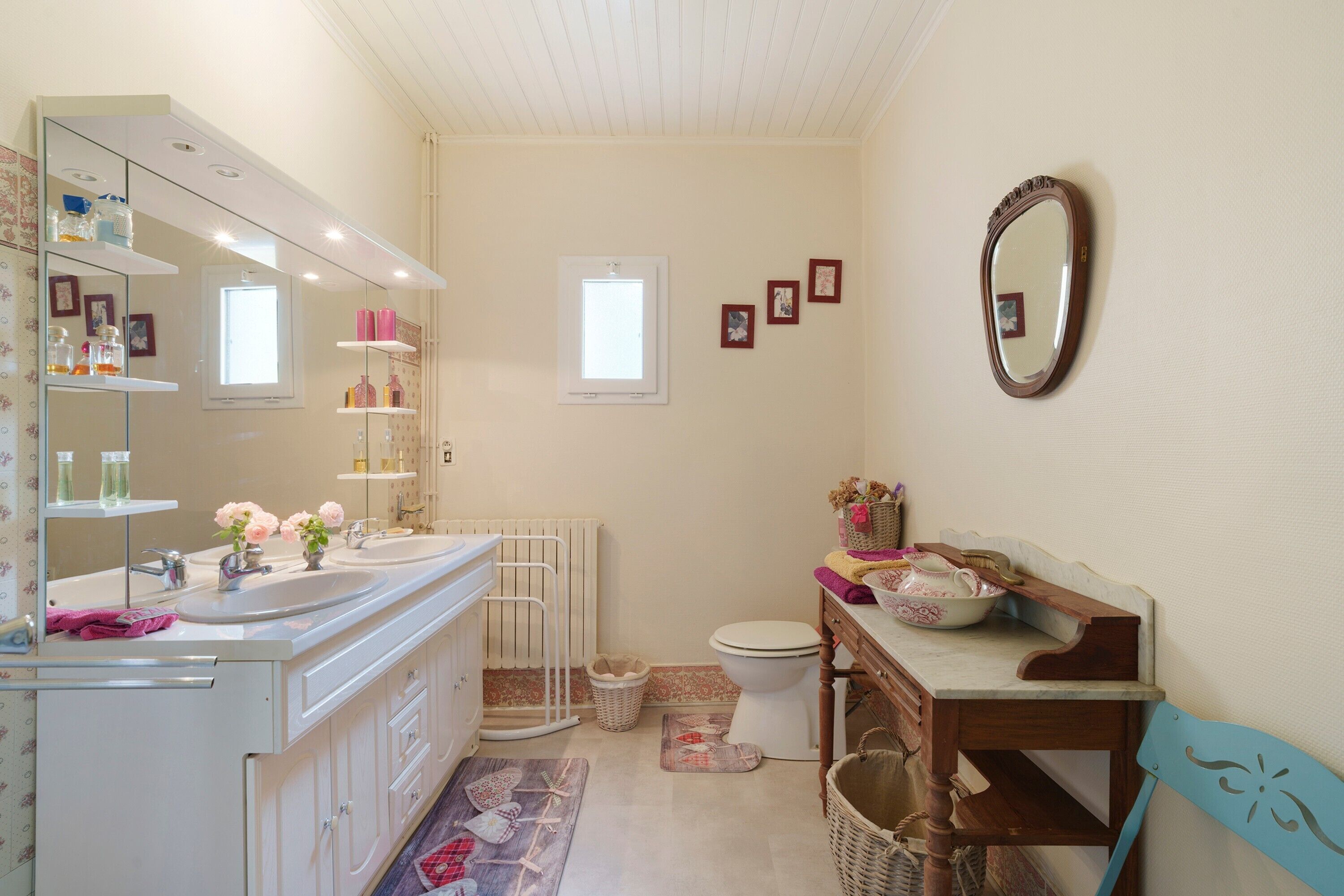 Une salle de bain avec un double vasque, un miroir, des toilettes et une petite fenêtre.