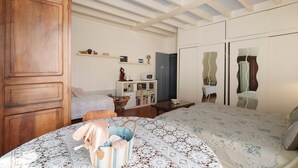 A bedroom with a wooden wardrobe, a bed with a floral bedspread, a small table, and a shelf with books and decorative items. - Bed and Breakfast 'Chambre Bleue' with Private Garden, Wi-Fi and Air Conditioning (Saint Aulaye-Puymangou)