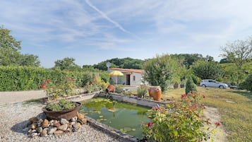 Un jardín con un estanque, una casa y un automóvil.