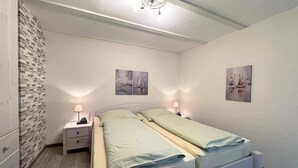 Et soveværelse med en dobbeltseng, to sengeborde med lamper, en væg med murstensmønster, og to billeder på væggen.
