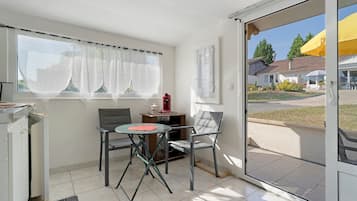 Ein Zimmer mit einer Schiebetür zum Außenbereich, einem Tisch mit einem Stuhl und einem Fenster mit transparenten Vorhängen.