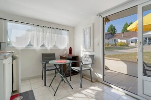 A room with a sliding glass door leading to an outdoor area, a small table with a chair, and a window with sheer curtains.