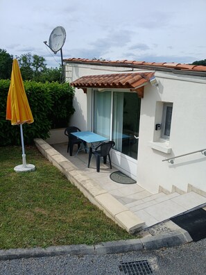 A small house with a tiled roof, a satellite dish, a blue table, and a yellow umbrella.