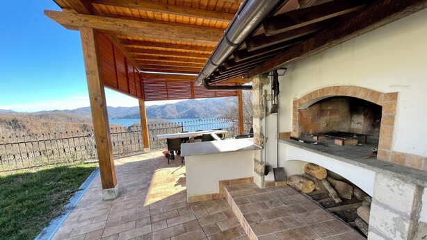 An outdoor patio with a stone-tiled floor, a brick oven, and a view of a lake and mountains. - Casale Nelli - Window on the Lake (Petrella Salto)
