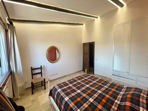 A bedroom with a bed, a chair, a mirror, and a door.