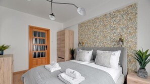 Un dormitorio con una cama grande, un armario de madera, una puerta con paneles de vidrio y un papel tapiz estampado.
