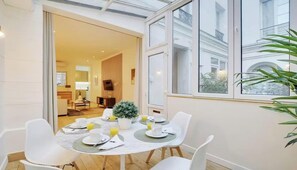 Ein Essbereich mit einem Tisch für vier Personen, einer Zimmerpflanze und Blick auf ein Gebäude durch große Fenster.