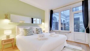 Habitación de hotel con cama, mesita de noche, espejo y ventana con vista a edificios.