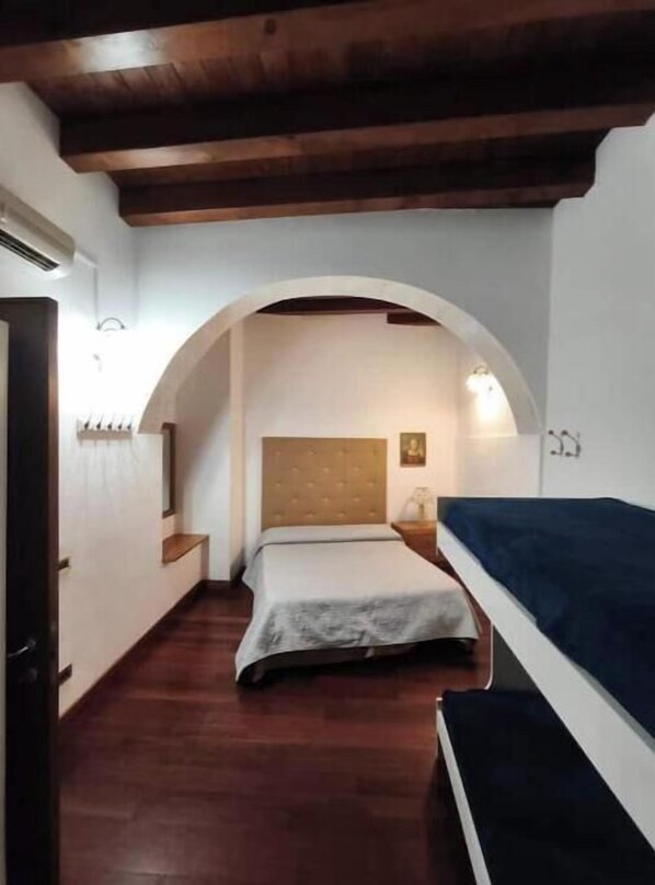 A bedroom with a bed, a nightstand, a wooden ceiling, and an arched doorway. - Ortigia Mare - Seafront Apartment with Balconies in the Historic Center (Siracusa)