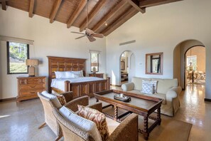 A spacious bedroom with a large bed, a wooden ceiling fan, a sofa, and a dining table. - Luxury 5BD With Stunning Ocean View - Casa Jalisco (San José del Cabo)