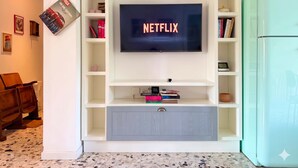 A living room with a TV mounted on a white entertainment unit, a bookshelf, and a teal refrigerator. - Casa Paolo Retro-design With Balcony Near Metro (Milan)