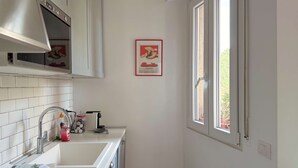 A kitchen with white cabinets, a stainless steel range hood, a window, and a framed picture on the wall. - Casa Paolo Retro-design With Balcony Near Metro (Milan)