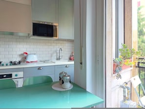 A kitchen with a microwave, stove, and cabinets. There is a window with a view of greenery. - Casa Paolo Retro-design With Balcony Near Metro (Milan)