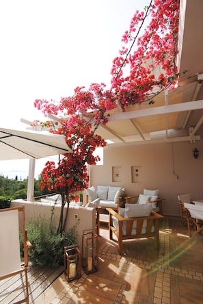 A sunlit patio with a wooden table, white chairs, and a pink flowering tree. - Porto Cheli 4bedroom Villa Plunge Pool Seaview 2 (Ermionida)