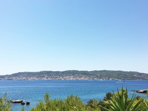 A coastal landscape with a clear view of the sea, a distant shoreline with buildings, and a boat in the water. - Porto Cheli 4bedroom Villa Plunge Pool Seaview 2 (Ermionida)
