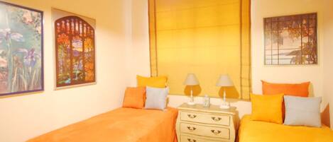 A room with two beds, a nightstand with lamps, and artwork on the walls.