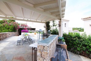 An outdoor patio with stone flooring, a white table with chairs, a stone bar, and a grill area. - Porto Cheli 4bedroom Villa Plunge Pool Seaview 2 (Ermionida)
