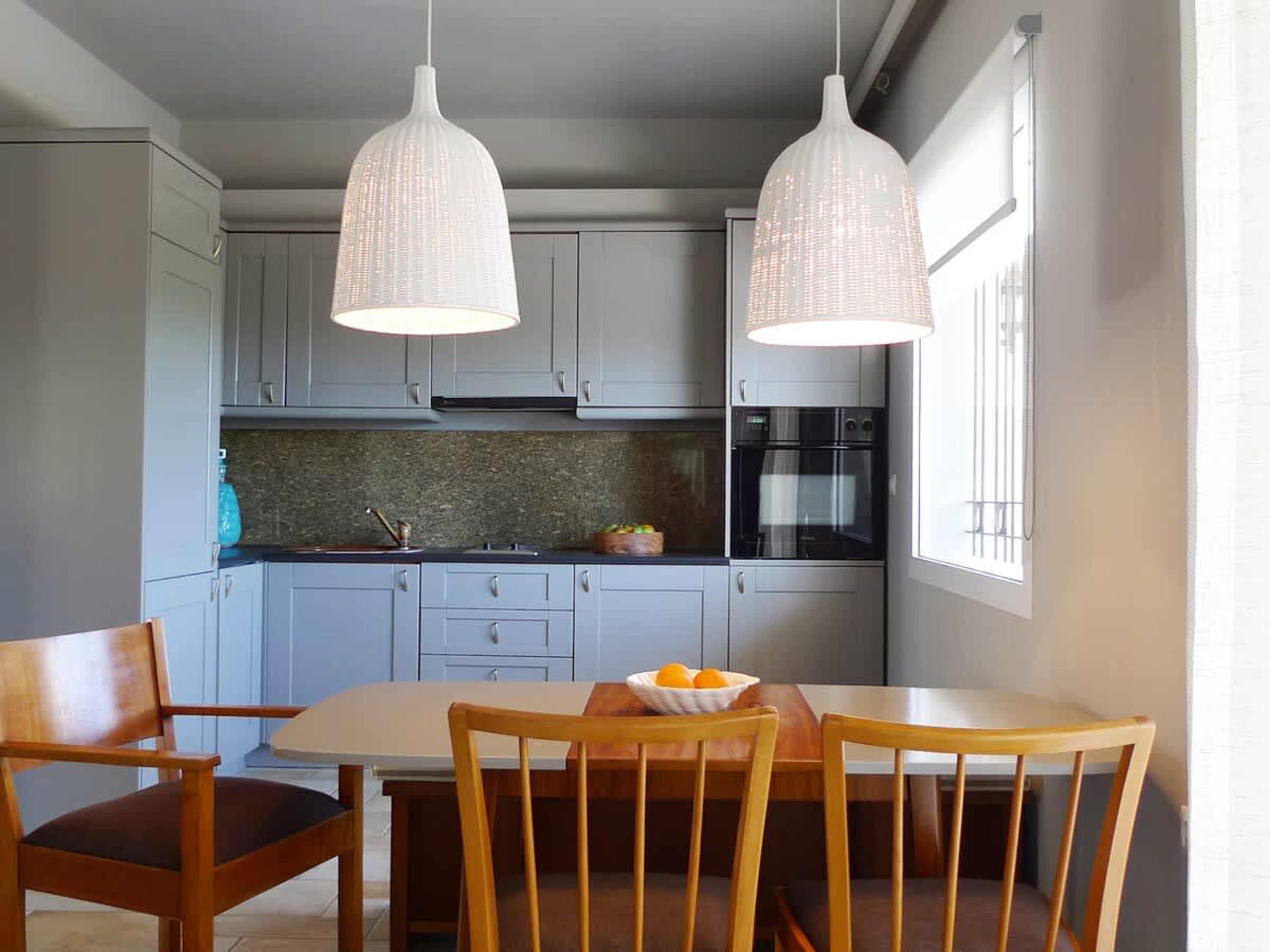 Cuina moderna amb armaris gris clars, taulell de granat i doble forn, il·luminada per dues làmpades penjants.