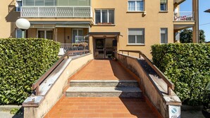 Ein mehrstöckiges Gebäude mit einem zentralen Eingang und Stufen, die hinauf führen, sowie einem Balkon im oberen Stockwerk.