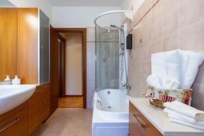 Ein modernes Badezimmer mit einer Badewanne, einer Duschkabine aus Glas, Holzschränken und einem Waschtisch mit Handtüchern.