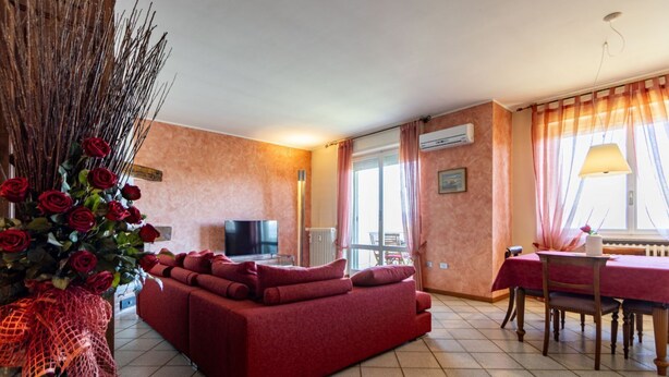 Ein Wohnzimmer mit einem roten Sofa, einem Fernseher, einem Esstisch mit Stühlen und einer Vase mit roten Rosen.