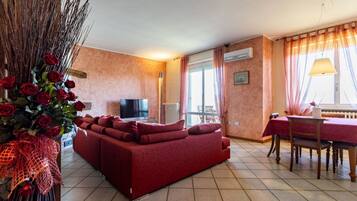 Ein Wohnzimmer mit einem roten Sofa, einem Fernseher, einem Esstisch mit Stühlen und einer Vase mit roten Rosen.