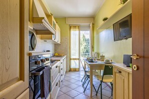 Cocina compacta con zona de comedor, televisor montado en la pared y puerta corrediza de vidrio que da a un balcón.