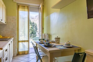A kitchen with a dining table set for two, a window with a view of trees, and a sliding door leading to an outdoor area.