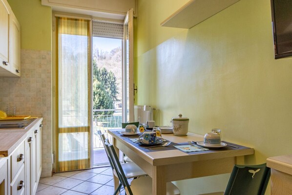 A kitchen with a dining table set for two, a window with a view of trees, and a sliding door leading to an outdoor area.