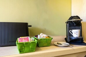 A kitchenette with a coffee maker, two green baskets, and a spoon on a wooden countertop.